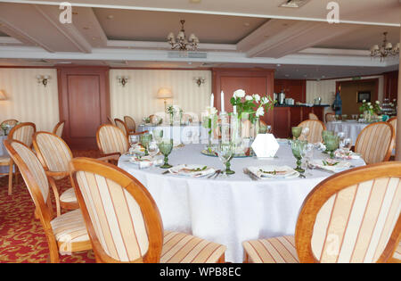 Table de salle à manger ronde, recouverte de tissu blanc, servi avec des lunettes et orné de fleurs, debout sur un tapis de couleur claire. Close-up Banque D'Images