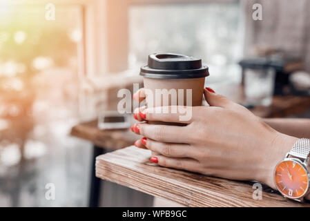 Tasse à café en papier pour aller dans woman's hands avec manucure rouge tout en étant assis dans le café. Banque D'Images