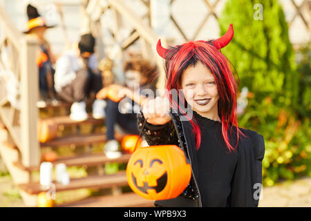 Portrait of cute little girl wearing costume Halloween à la caméra tout en se posant à l'extérieur holding pumpkin panier dans trick or treat saison, copy space Banque D'Images