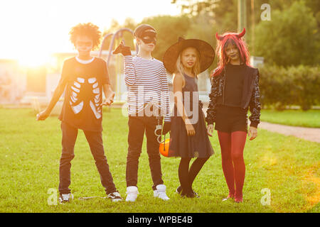 Groupe multi-ethnique des enfants portant des costumes de Halloween à la caméra tout en se posant à l'extérieur éclairée par la lumière du soleil, copy space Banque D'Images