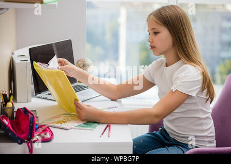 Fille de l'école devoirs avec l'étude de livres à couverture jaune. Home intérieur. Girl lit attentivement manuel. Banque D'Images