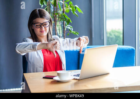 L'aversion. Portrait d'insatisfaits belle brunette élégante jeune femme à lunettes assis, la regardant un écran d'ordinateur portable sur appel vidéo avec thumbs n Banque D'Images