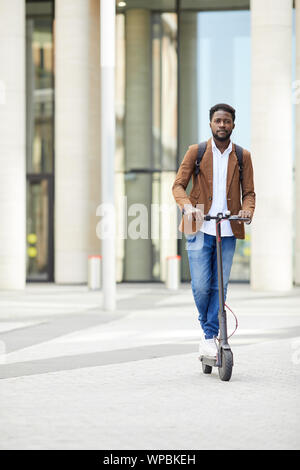 Portrait de l'homme afro-américain contemporain riding scooter électrique et looking at camera lors des trajets dans les rues de la ville, copy space Banque D'Images