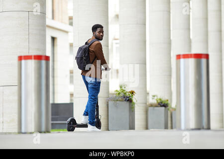 Large angle portrait of contemporary African man riding scooter électrique en ville rue et looking at camera, copy space Banque D'Images