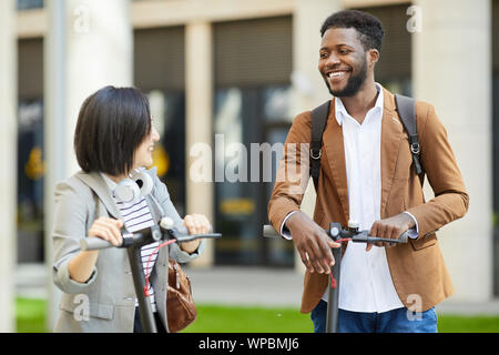 Groupe multiethnique de cheerful young people riding scooter électrique en ville rue et souriant heureusement regarder, copy space Banque D'Images