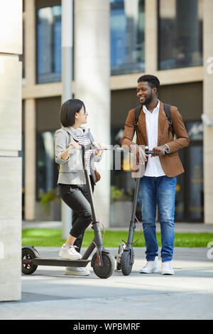 Portrait de jeune contemporain couple riding scooter électrique en ville rue et souriant heureusement regarder, copy space Banque D'Images