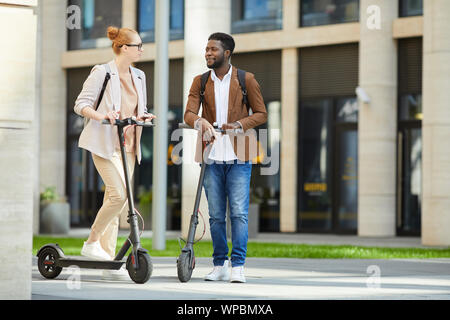 Portrait de jeunes contemporains équitation des scooters électriques dans la rue ville et souriant heureusement regarder, copy space Banque D'Images