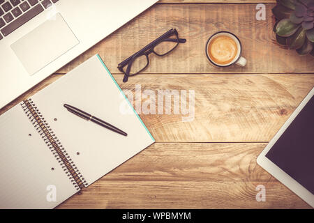 Bureau en bois rustique avec ordinateur portable, portable, un stylo, lunettes, tasse de café et tablette ordinateur. Espace de travail moderne avec copie espace. Effet tonifiant du filtre. Banque D'Images