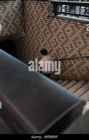 MATSUYAMA, JAPON - Jul 30, 2019 : une ligne verticale de sélective une vieille femme marchant dans les escaliers avec une main courante sur un mur de briques Banque D'Images