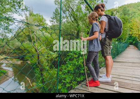 Mère et fille debout sur le pont suspendu en bois et à la recherche à la petite rivière ci-dessous Banque D'Images