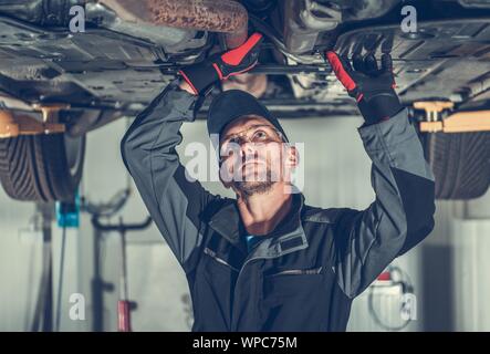 Vérifier la sonde lambda d'échappement. Mécanicien Auto Service professionnel à problèmes avec un véhicule moderne pendant la vérification de la voiture sous le chariot. Banque D'Images