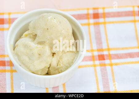 Maison vegan jaune banane et mangue dairy-free gelato la crème glacée dans un bol avec une cuillère en porcelaine, fond rose. L'espace de copie, selective focus. Banque D'Images
