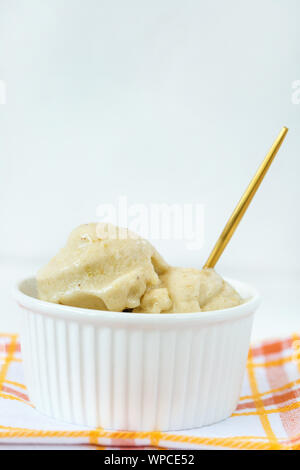 Maison vegan jaune banane et mangue dairy-free gelato la crème glacée dans un bol avec une cuillère en porcelaine, fond rose. L'espace de copie, selective focus. Banque D'Images