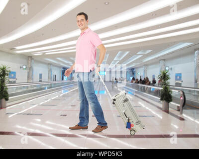 Homme tirant une valise et souriant dans un terminal d'aéroport Banque D'Images