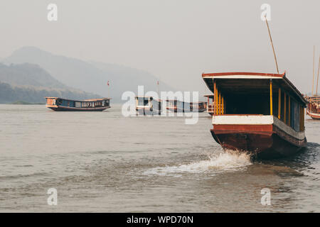 Bateaux traditionnels en bois laotien lent sur le fleuve du Mékong près de Luang Prabang, Laos, au coucher du soleil. Arrière-plan sur la montagne Banque D'Images