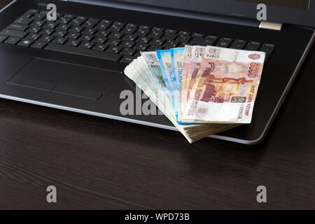 Fédération de monnaie de papier pliée en ventilateur disposés sur clavier d'ordinateur portable. Table marron foncé avec copie espace. Haut angle view. Billets de différentes dénominations. Banque D'Images