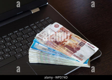 Les paiements en espèces pour le travail informatique concept. Fédération de monnaie de papier pliée en ventilateur disposés sur clavier d'ordinateur portable. Table marron foncé avec copie espace. Différents Banque D'Images