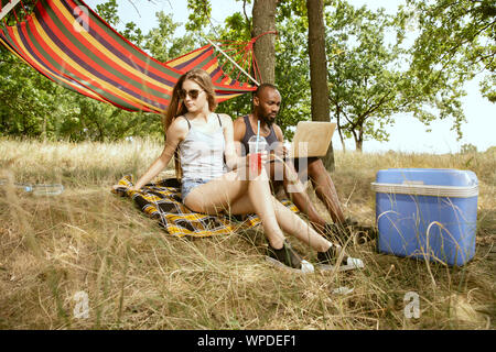 Jeune couple romantique international multi-ethnique en plein air sur la prairie en journée ensoleillée. L'homme afro-américains et caucasian woman having picnic ensemble. Concept de relation, l'été. Banque D'Images