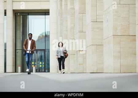 Longueur totale de portrai deux personnes marchant dans la rue de la ville, l'accent sur l'homme afro-américain équitation scooter électrique, copy space Banque D'Images