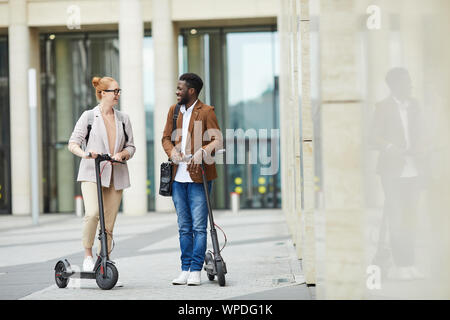 Portrait of mixed race woman riding scooters en alectric ville rue et souriant joyeusement, copy space Banque D'Images