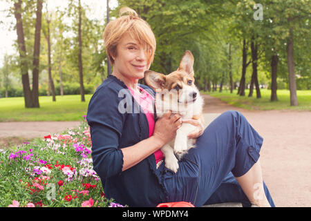 Happy woman sitting with dog on bench en fleurs parc d'été Banque D'Images