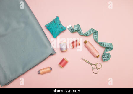 Outils de couture, tricot bleu pour la couture à l'aiguille, ciseaux et des bobines de fil de couleur sur un fond rose avec copie espace pour le texte Banque D'Images