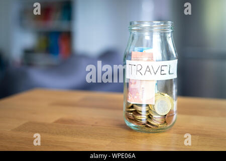 Verre transparent pot étiqueté voyage avec les billets et pièces en euro à l'intérieur. Pièces en Euro à l'extérieur sur le dessus d'une table en bois. Banque D'Images