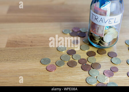 Verre transparent pot étiqueté voyage avec les billets et pièces en euro à l'intérieur. Pièces en Euro à l'extérieur sur le dessus d'une table en bois. Banque D'Images