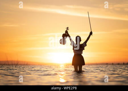 Girl playing violin sur l'eau avec fond coucher de soleil Banque D'Images