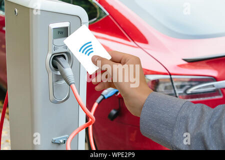 Un homme paie pour la recharge d'une voiture électrique. Banque D'Images