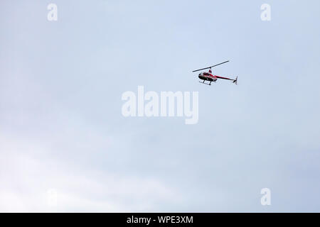 Un hélicoptère rouge plaisir vole dans le ciel au cours d'une visite à pied contre un ciel gris. Le transport aérien. Banque D'Images