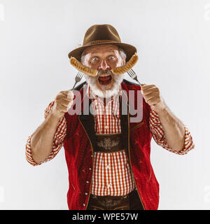 Portrait of senior man in hat Oktoberfest, le port du vêtement traditionnel bavarois. Pleine longueur mâle tourné au studio sur fond blanc. La célébration, vacances, festival concept. Manger des saucisses. Banque D'Images