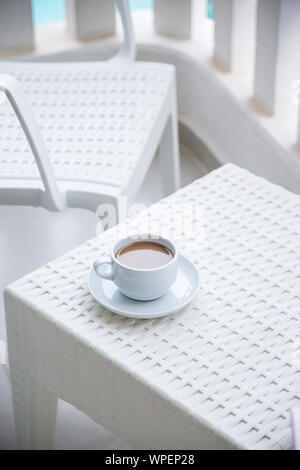 Une tasse de café avec du lait dans un bol blanc sur le balcon de l'hôtel donnant sur les eaux bleues de la piscine au milieu des palmiers Banque D'Images
