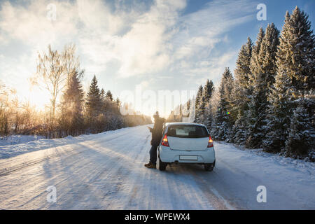 Jeune homme est debout près de la voiture sur une route d'hiver. Banque D'Images