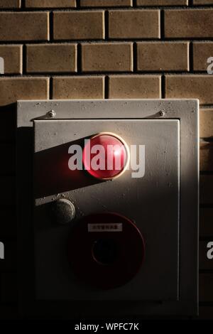 Gros plan vertical d'un voyant d'alarme rouge de sécurité allumé une boîte grise sur un mur de briques Banque D'Images