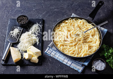 Close-up of belrom e pepe, spaghetti mélangée avec du fromage râpé et saupoudrées de poivre noir fraîchement moulu dans une poêle avec une fourchette. Ingrédients sur un bl Banque D'Images