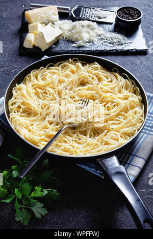 Close-up of belrom e pepe, pâtes mélangées avec du fromage pecorino râpé et saupoudrées de poivre noir fraîchement moulu dans une poêle avec une fourchette, vue verticale Banque D'Images