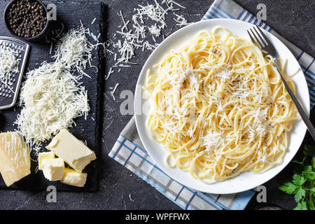 Close-up of belrom e pepe, creany les pâtes mélangées avec du fromage pecorino râpé et saupoudrées de poivre noir fraîchement moulu sur une plaque blanche avec une fourchette. gra Banque D'Images