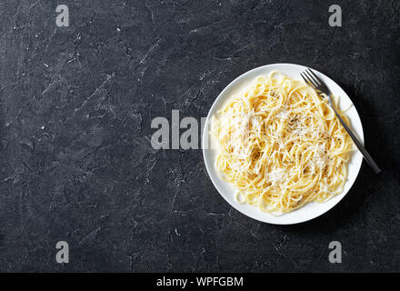 Belrom e pepe, spaghetti mélangée avec du fromage pecorino râpé et saupoudrées de poivre noir fraîchement moulu sur une plaque blanche avec une fourchette, vue de dessus, f Banque D'Images