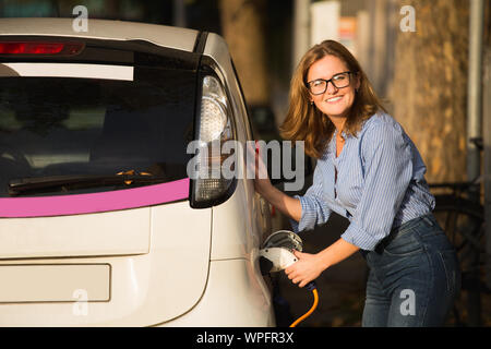 Jeune femme se charge carsharing voiture électrique. Banque D'Images