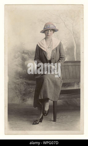 Au début des années 1900, la carte postale originale du portrait de studio teinté d'une jolie jeune femme portant une jupe et une veste typiques de l'époque, un chapeau et éventuellement une broche chérie du Royal Flying corps (RFC) sur son col, tenant des gants et un grand locket, Gravesend, Kent, R.-U. vers 1915 Banque D'Images