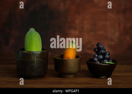 La nature morte la banane, carotte, raisins sont dans une tasse de poterie sur table en bois rustique, choisissez un point de convergence. Banque D'Images