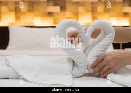 Close-up de mettre les mains de oiseaux cygnes plié les serviettes de bain blanc frais sur le drap de lit dans l'hôtel. Banque D'Images