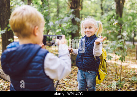 Les enfants d'âge préscolaire Caucasian frère et soeur de prendre des photos de l'autre caméra sur téléphone mobile dans le parc forestier de l'automne. thème de hobby et active Banque D'Images