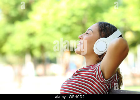 Side view portrait of a happy mixed race woman resting assis sur un banc dans un parc Banque D'Images