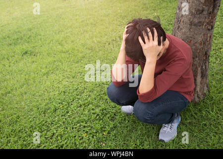 Une personne porte une chemise rouge, saisit sa tête avec le stress dans le jardin au coucher du soleil. Santé mentale, concept de dépression. Banque D'Images