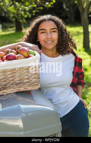 Belle happy mixed race African American girl biracial adolescent femme jeune femme souriante avec des dents parfaites dans un verger s'appuyant sur un tracteur wi Banque D'Images