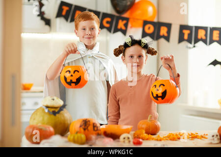 Portrait of cute boy and girl holding lanternes et smiling at camera tout en visitant Halloween party Banque D'Images