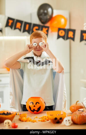 Portrait de funny boy habillé en costume faire un visage tout en se tenant près de la table avec des lanternes à Halloween party Banque D'Images