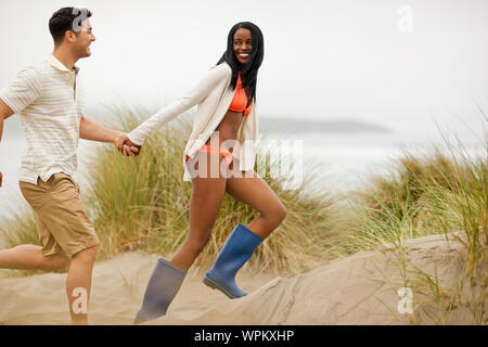 Smiling young couple holding hands tout en courant à travers les dunes de sable. Banque D'Images